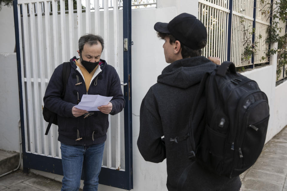 A high school teacher checks a document stating a negative COVID-19 self-test outside a school at Glyfada suburb, west of Athens, Monday, April 12, 2021. Home tests have been distributed to teachers and students aged 16-18, as authorities reopened high schools for students in the final three grades on Monday. (AP Photo/Yorgos Karahalis)