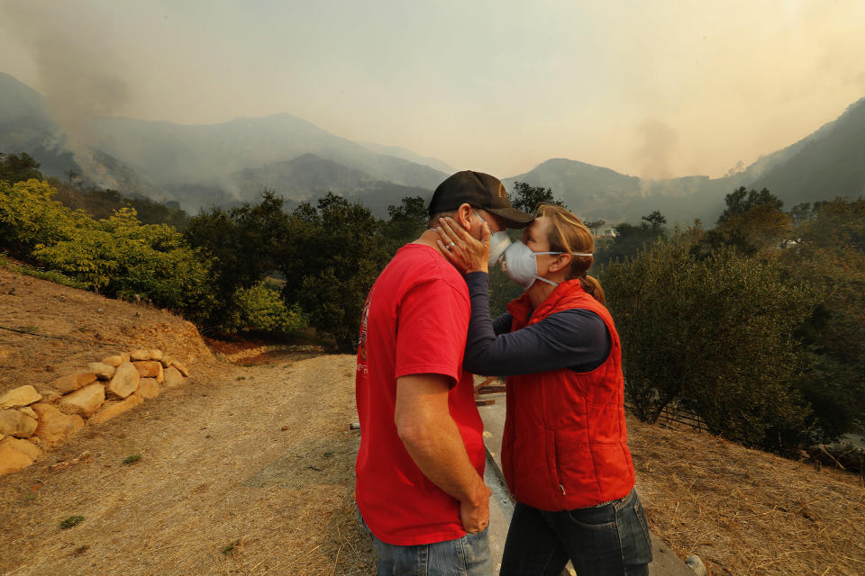 <p>Dan Bellaart and his wife Mary McEwen comfort each other in the back yard of their home that includes an avocado ranch on 9 acres of land on Toro Canyon Rd. as the Thomas fire burns in the background on Dec., 11, 2017 in Montecito, Calif. They have lived here since 2002. (Photo: Mel Melcon/Los Angeles Times via Getty Images) </p>