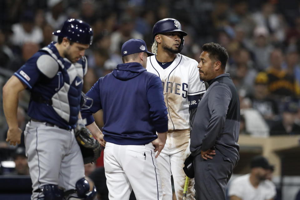 San Diego Padres' Fernando Tatis Jr., second from right, talks with manager Andy Green, second from left, and a trainer during an at-bat as Tampa Bay Rays catcher Mike Zunino stands at left during the sixth inning of a baseball game Tuesday, Aug. 13, 2019, in San Diego. (AP Photo/Gregory Bull)