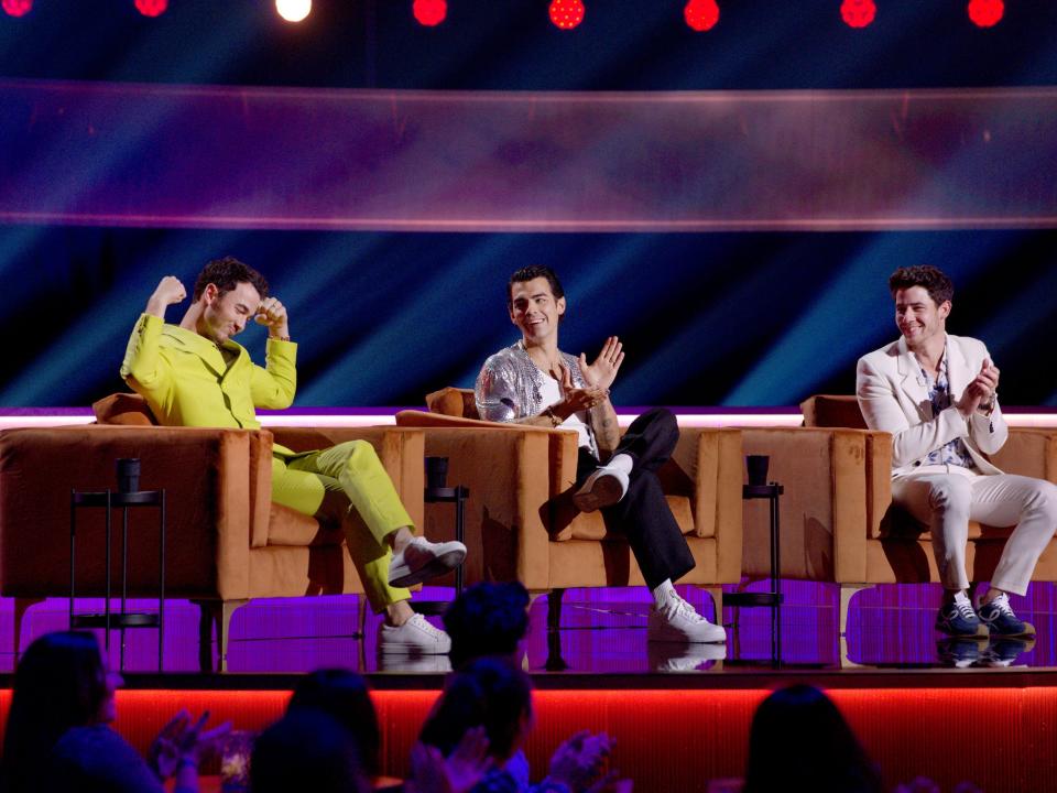 Kevin Jonas, Joe Jonas, and Nick Jonas sitting on couches during the "Jonas Brothers Family Roast."
