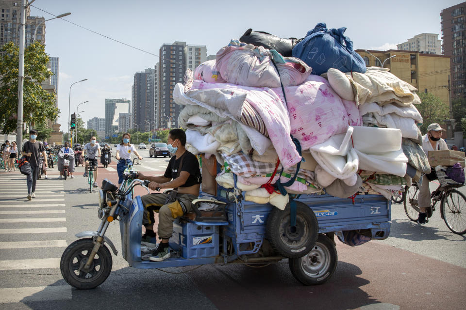 A man wearing a face mask to protect against the new coronavirus drives a cart loaded with fabric in Beijing, Tuesday, July 14, 2020. Health experts are warning that outbreaks brought under control with shutdowns and other forms of social distancing are likely to flare again as precautions are relaxed. (AP Photo/Mark Schiefelbein)