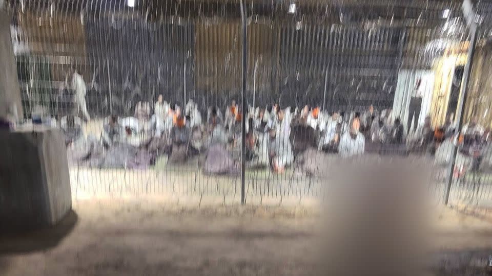 A leaked photograph of an enclosure where detainees in gray tracksuits are seen blindfolded and sitting on paper-thin mattresses. CNN was able to geolocate the hangar in the Sde Teiman facility. A portion of this image has been blurred by CNN to protect the identity of the source. - Obtained by CNN