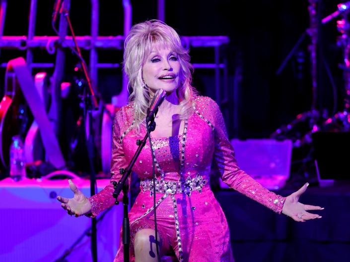 Dolly Parton with high hair and a bright pink costume, singing on stage.