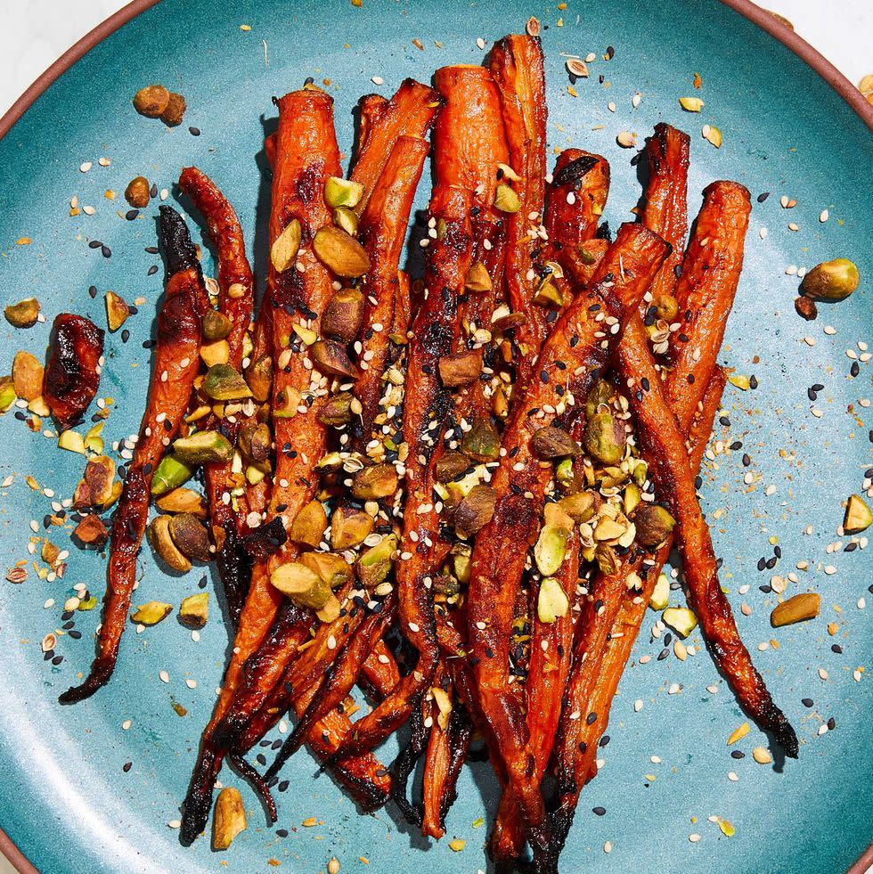 miso roasted carrots topped with pistachios and black and white sesame seeds on a teal plate