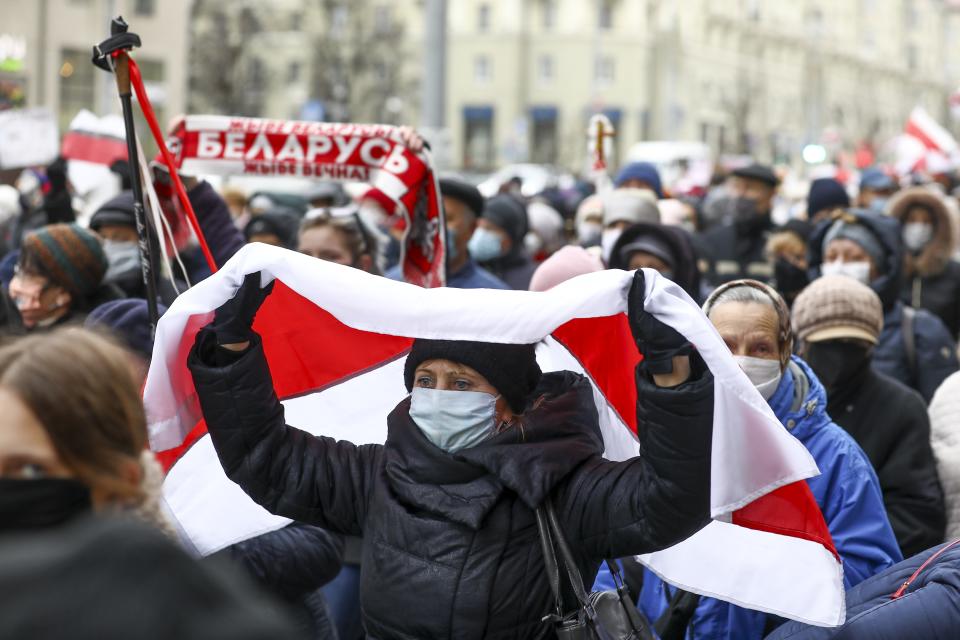 A woman covers herself by an old Belarusian national flag attends a pensioners' opposition rally to protest the official presidential election results in Minsk, Belarus, Monday, Nov. 16, 2020. Crowds of retirees marched down the streets of the Belarusian capital on Monday, demanding the resignation of the country's authoritarian president and to end the government crackdown on peaceful protesters. (AP Photo)