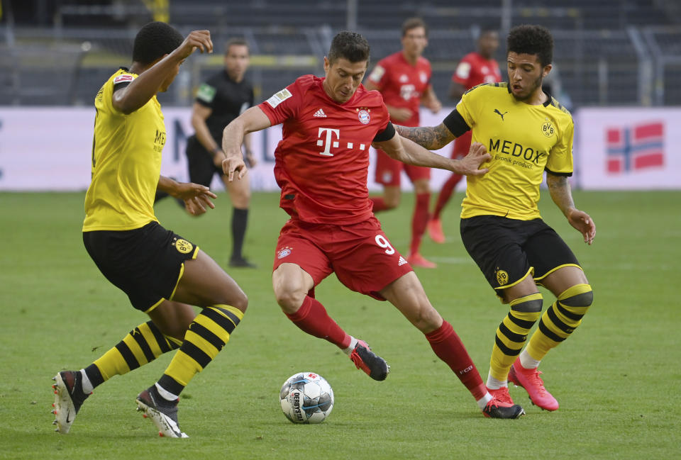 Munich's Robert Lewandowski, center, and Dortmund's Jadon Sancho, right, challenge for the ball during the German Bundesliga soccer match between Borussia Dortmund and FC Bayern Munich in Dortmund, Germany, Tuesday, May 26, 2020. The German Bundesliga is the world's first major soccer league to resume after a two-month suspension because of the coronavirus pandemic. (Federico Gambarini/DPA via AP, Pool)