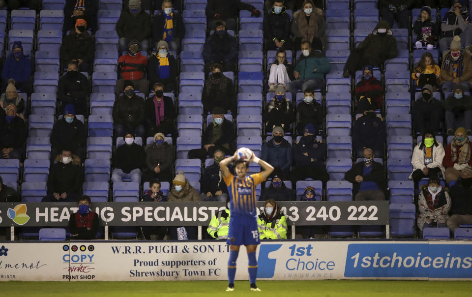 Shrewsbury Town's Charlie Daniels, center, takes a throw-in as the fans watch during Championship soccer match at Montgomery Waters Meadow, Shrewsbury, England, Wednesday Dec. 2, 2020. A small number of fans are being welcomed back into soccer games as the second national lockdown is relaxed Wednesday, with COVID-19 numbers closely watched during the restriction change. (Nick Potts/PA via AP)