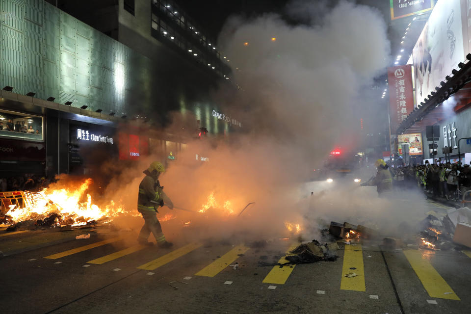 Firefighters put out fire by protesters during a protest in Mong Kok, in Hong Kong on Friday, Sept. 6, 2019. The ratings agency Fitch on Friday cut Hong Kong's credit rating and warned that conflict with anti-government protesters was hurting the image of its business climate. (AP Photo/Kin Cheung)