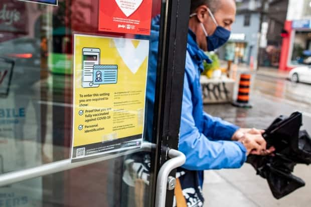 A patron leaves a fast food restaurant on Queen Street in Toronto, past a sign outlining proof of vaccination requirements on Sept. 22. Patrons of dine-in restaurants, nightclubs, gyms, sports facilities and other venues must present a receipt of full vaccination along with government identification. (Evan Mitsui/CBC - image credit)