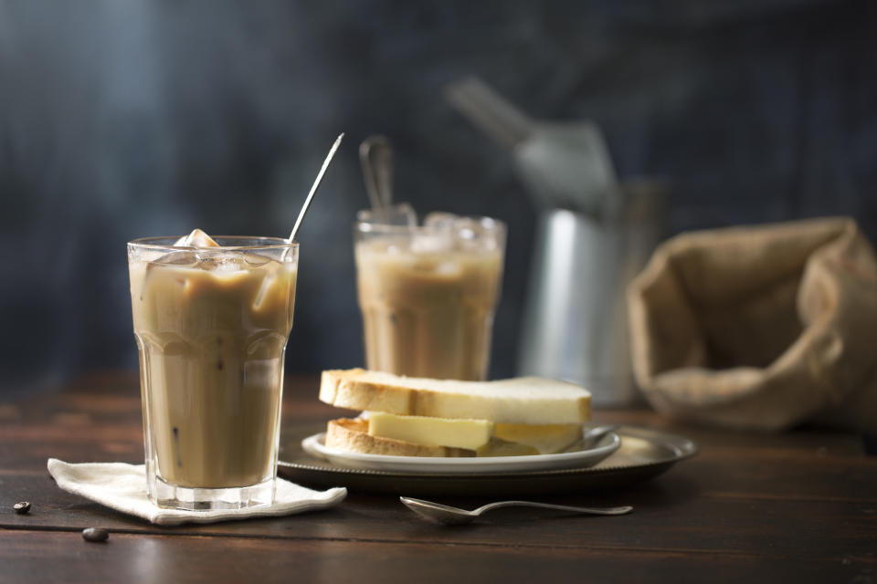 South east asian Malaysian Singaporean local traditional iced white coffee (coffee with milk) in vintage glass. Served with traditional coconut jam and butter toast and soft half boiled egg in bowl. Rustic moody wooden background.