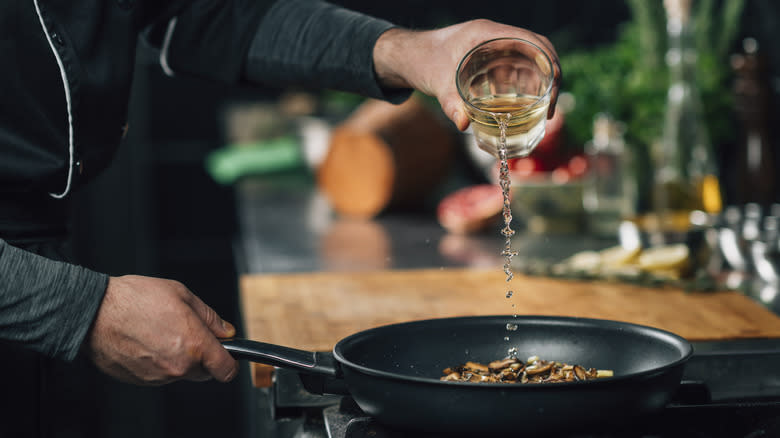 chef adding wine to mushrooms