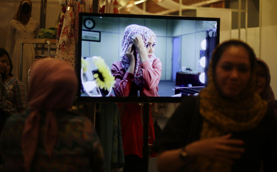 In this Thursday, May 30, 2013 photo, Indonesian Muslim women walk past a TV screen showing a video tutorial on how to wear a hijab or headscarf, during Islamic Fashion Fair in Jakarta, Indonesia. Indonesia is the world's most populous Muslim country, but most people follow a moderate form of the religion. Many women wear bright and creative headscarves along with brand-name jeans and long-sleeved fitted shirts. (AP Photo/Dita Alangkara)
