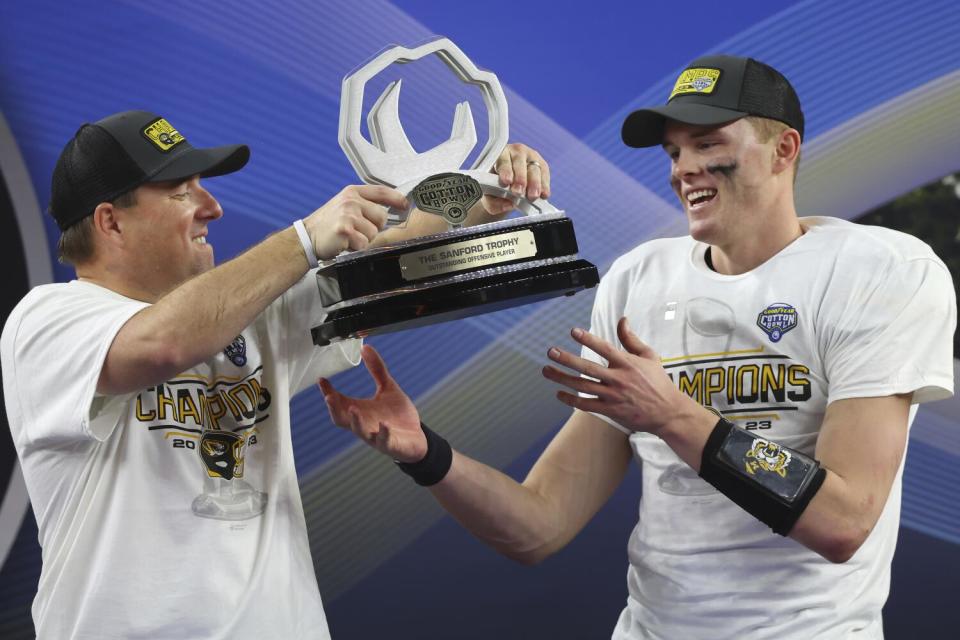 Eliah Drinkwitz and Brady Cook celebrate with a trophy.