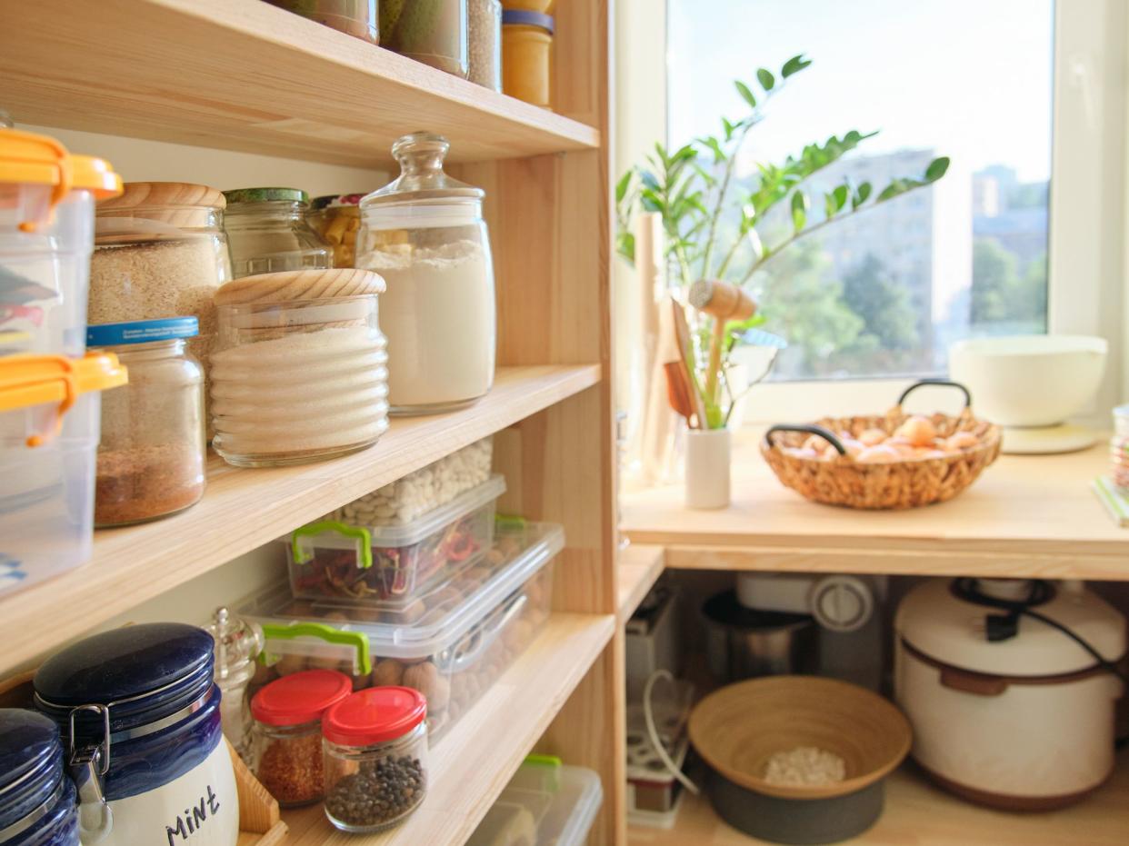 Wooden shelves with food and utensils, kitchen appliances in the pantry.