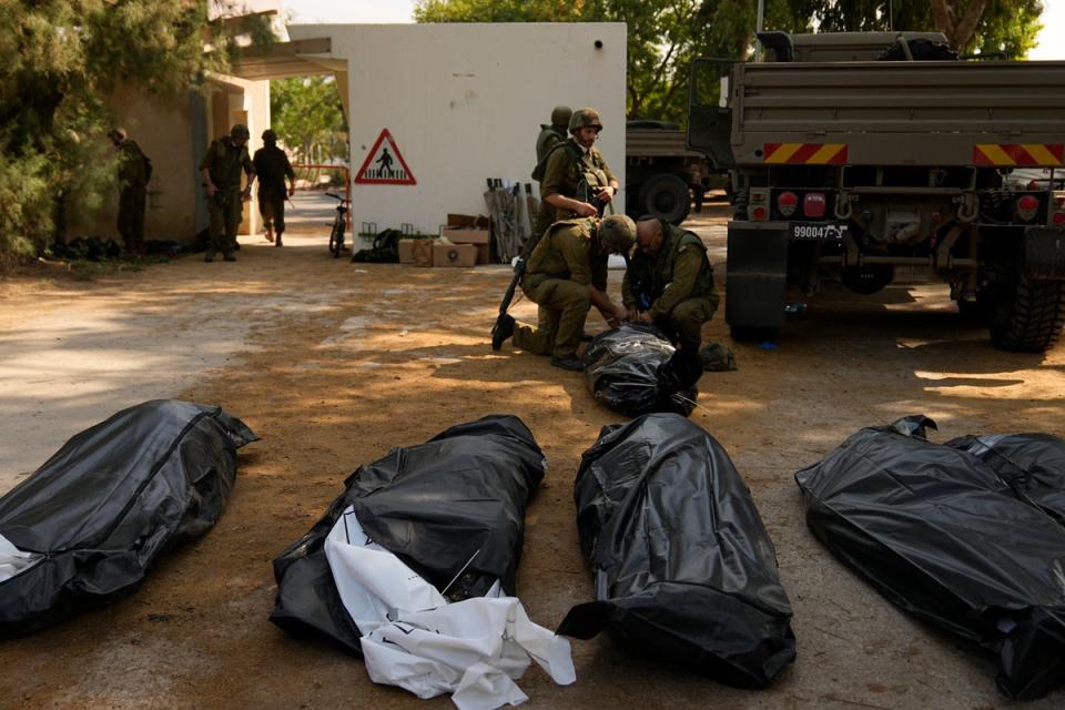Israeli soldiers stand next to the bodies of Israelis killed by Hamas militants in kibbutz (AP)