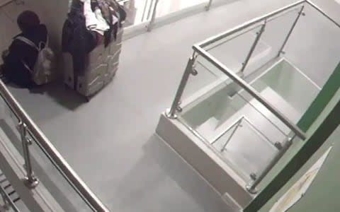 A woman sits on the stairs inside Grenfell Tower with a suitcase behind her, unaware the block of flats is being engulfed by flames above her