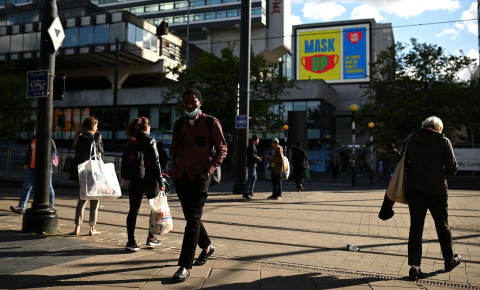 A man wears a face mask under his chin as he walks near a sign urging people "Mask up" in Manchester, northwest England on August 3, 2020, following a rise in the number of COVID-19 cases in the region. - Britain on Friday "put the brakes on" easing lockdown measures and imposed new rules on millions of households in northern England, following concerns over a spike in coronavirus infections. The government increased regional lockdown measures -- under which people from different households are banned from meeting indoors -- for some four million people across Greater Manchester and parts of Lancashire and Yorkshire. (Photo by Oli SCARFF / AFP) (Photo by OLI SCARFF/AFP via Getty Images)