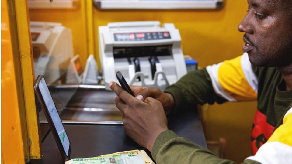 An agent conducts a mobile money transfer transaction with a customer at a kiosk in Kampala, Uganda, Wednesday, Aug. 16, 2023.