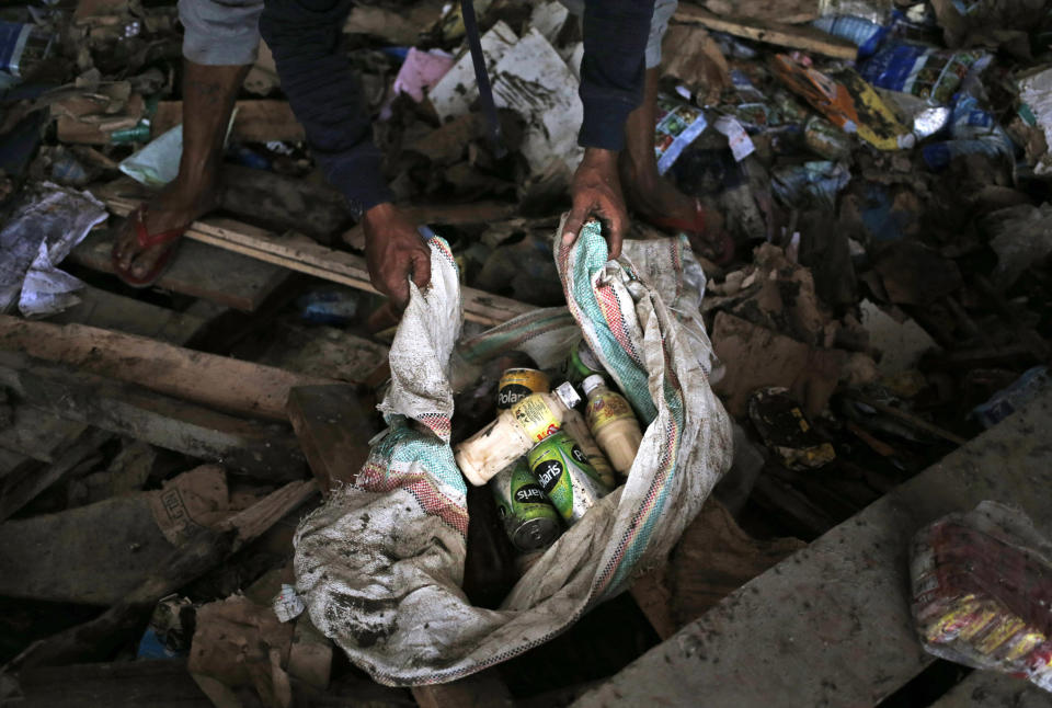 A man put beverages scavenged from an abandoned warehouse into a sack at an earthquake and tsunami-affected area in Palu, Central Sulawesi, Indonesia Indonesia, Wednesday, Oct. 3, 2018. Clambering over the reeking pile of sodden food or staking out a patch of territory, people who had come from devastated neighborhoods and elsewhere in the remote Indonesian city pulled out small cartons of milk, soft drinks, rice, candy and painkillers from the pile as they scavenge for anything edible in the warehouse that tsunami waves had pounded. (AP Photo/Dita Alangkara)