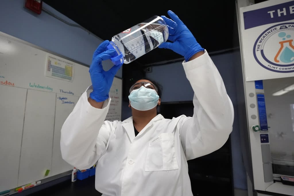 Person in a medical mask and gloves holds up a bottle of water to check it for clarity