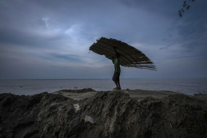 FILE - A villager carries material salvaged from his home before it was washed away by erosion of the river Brahmaputra at Murkata village, northeastern Assam state, India, Oct. 9, 2022. India officially takes up its role as chair of the Group of 20 leading economies for the coming year Thursday, Dec. 1 and it's putting climate at the top of the group's priorities. (AP Photo/Anupam Nath, File)