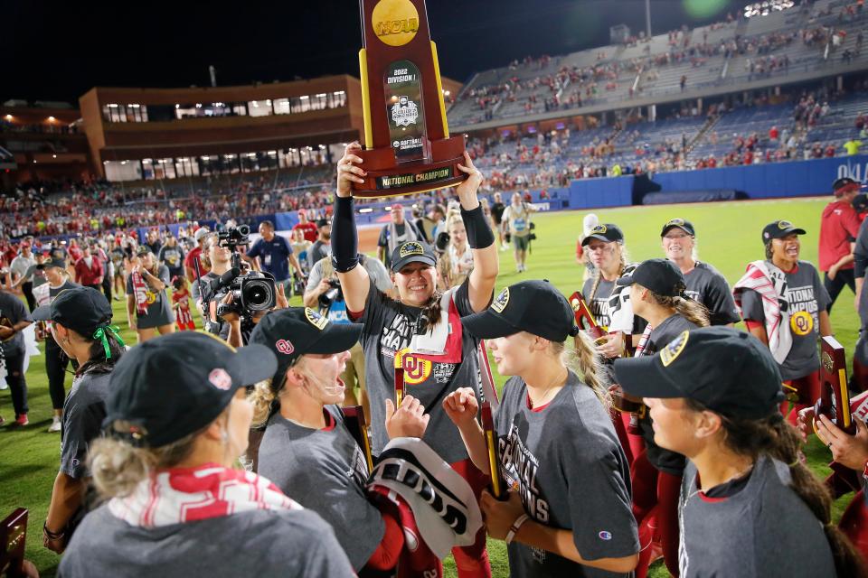 Oklahoma's Hope Trautwein holds the trophy as Oklahoma players celebrate their win over Texas to win the NCAA softball title with a Women's College World Series series sweep over the Texas Longhorns at USA Softball Hall of Fame Stadium in Oklahoma City, Thursday, June 9, 2022. 