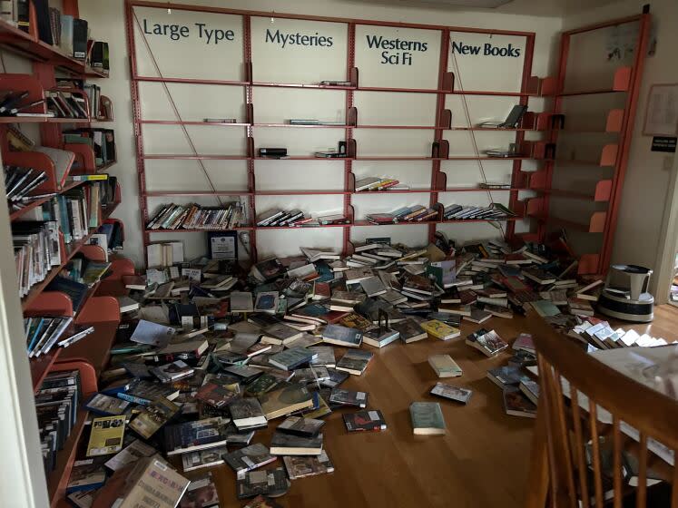 AA view of a room lined with near-empty bookshelves and books strewn all round on the floor.