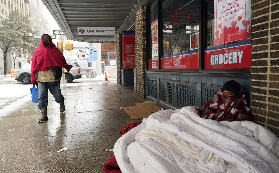 FILE - In this Feb. 18, 2021, file photo, a woman living on the streets uses blankets to keep warm in downtown San Antonio. Snow, ice and sub-freezing weather continue to wreak havoc on the state's power grid and utilities. (AP Photo/Eric Gay)