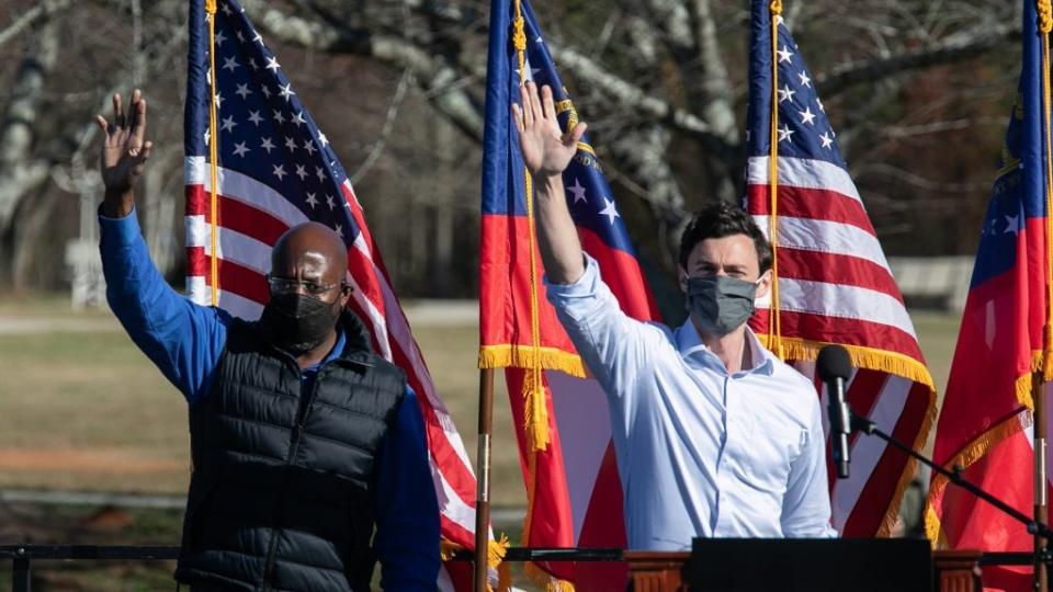 Democratic U.S. Senate candidates Raphael Warnock (L) and Jon Ossoff wave to the crowd during an outdoor drive-in rally on December 5, 2020 in Conyers, Georgia. (Photo by Jessica McGowan/Getty Images)