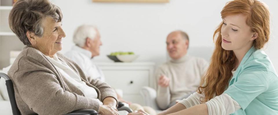 Young caregiver taking care of older disabled woman in nursing home