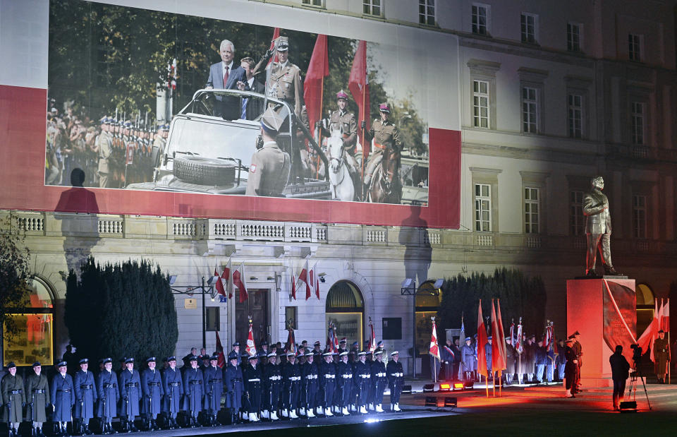 A Polish Army guard of honor stands next to the monument of the late Polish President Lech Kaczynski, who died in a 2010 plane crash, in Warsaw, Poland, Saturday, Nov. 10, 2018, during the official unveiling ceremony being a part of the centennial observances marking 100 years of Polish independence. The photo on the building shows Lech Kaczynski during a military ceremony. (AP Photo/Alik Keplicz)