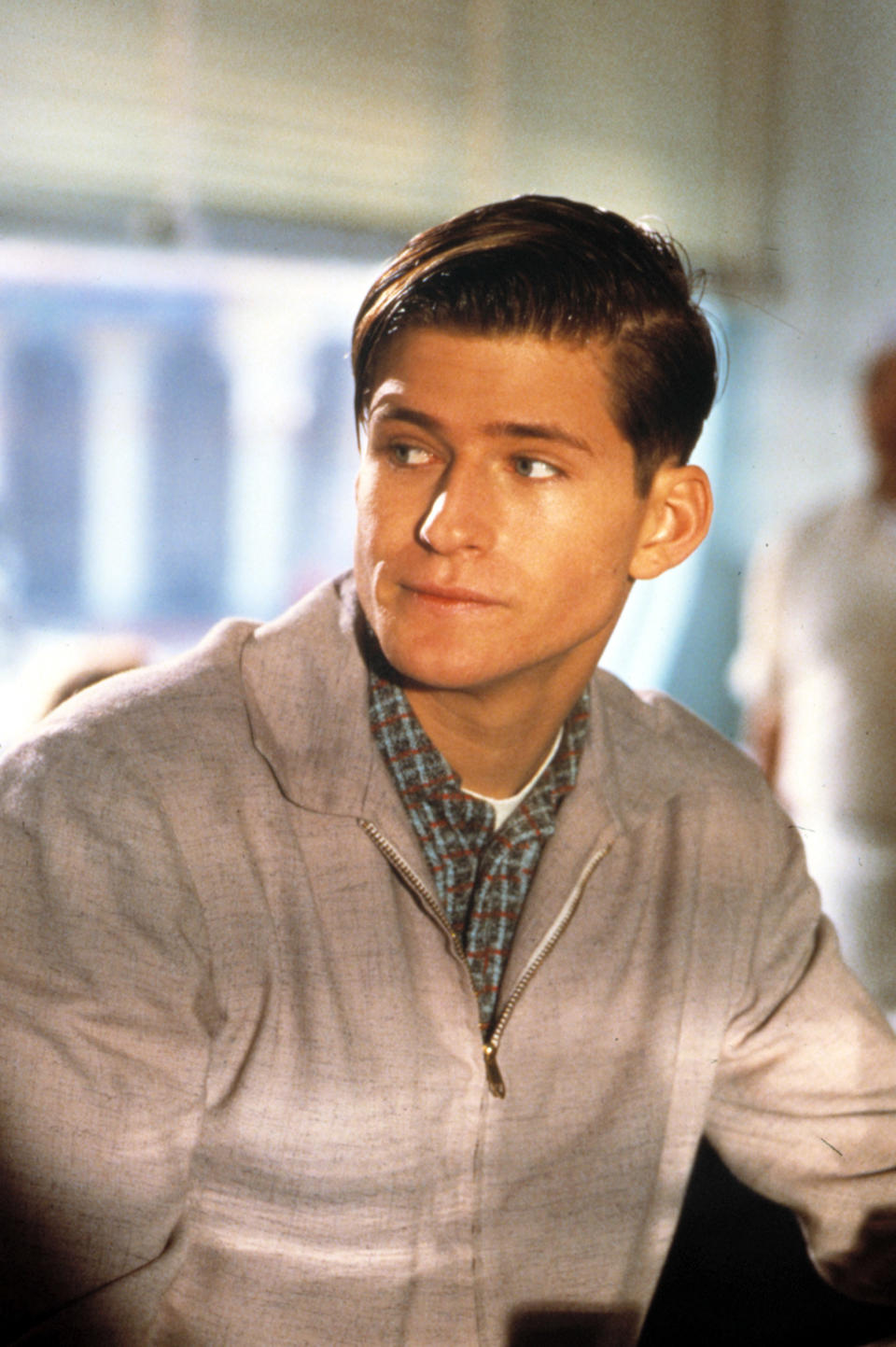 Crispin Glover in a scene from "Back to the Future," wearing a light jacket over a plaid shirt, with a retro hairstyle