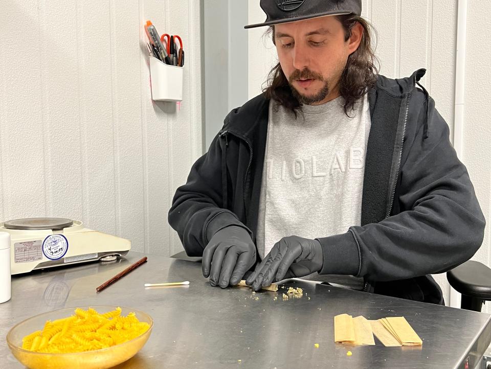 Photograph of Thomas Indigaro looking downwards as he rolls a joint on the table wearing gloves.