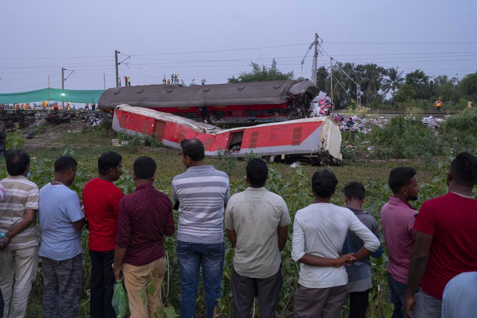 People look at the mangled wreckage of the two passenger trains that derailed Friday in Balasore district, in the eastern state of Orissa, India, Sunday, June 4, 2023. The derailment in eastern India that killed 275 people and injured hundreds was caused by an error in the electronic signaling system that led a train to wrongly change tracks and crash into a freight train, officials said Sunday. (AP Photo/Rafiq Maqbool)