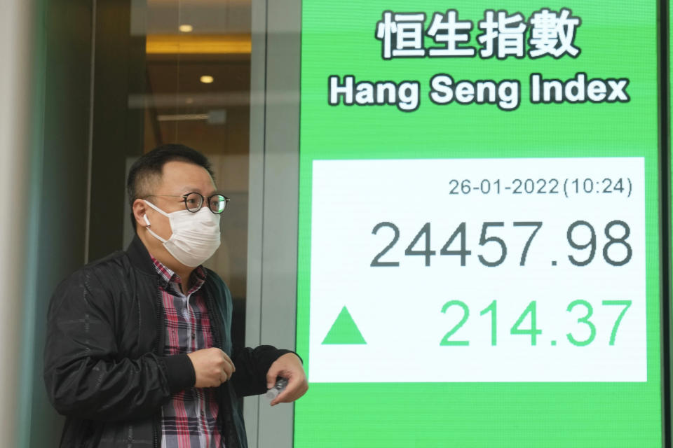 A man wearing a face mask walks past a bank's electronic board showing the Hong Kong share index in Hong Kong, Wednesday, Jan. 26, 2022. Asian shares were mixed in muted trading Wednesday as many stayed on the sidelines ahead of a U.S. Federal Reserve meeting that will indicate how aggressive it will be in fighting inflation. (AP Photo/Kin Cheung)