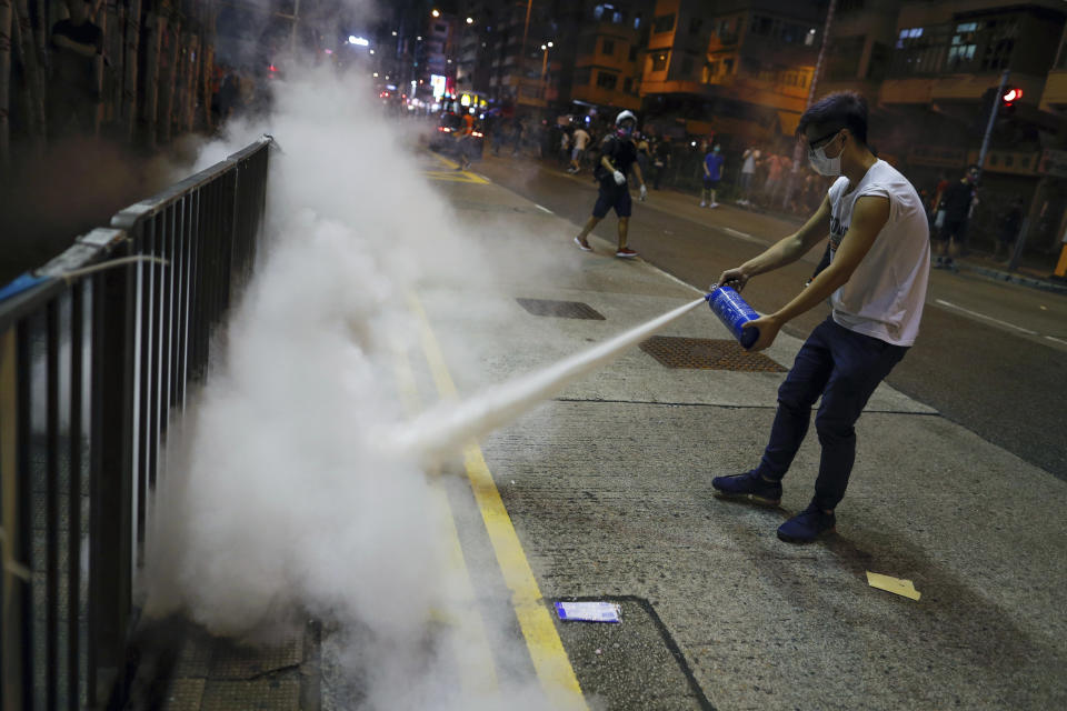 A man uses a fire extinguisher to put out a tear gas canister as they confront police in Hong Kong on Wednesday, Aug. 14, 2019. German Chancellor Angela Merkel is calling for a peaceful solution to the unrest in Hong Kong amid fears China could use force to quell pro-democracy protests. (AP Photo/Vincent Yu)