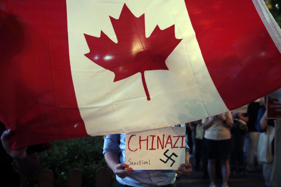 A pro-Hong Kong protester holds a sign while standing behind a Canadian flag during a gathering to honor a woman who suffered a serious eye injury in a recent protest, Friday, Aug. 30, 2019, in Hong Kong. Police have appealed to Hong Kong residents to stay from any non-authorized rallies on Saturday after authorities banned a major march, warning that those caught could face a five-year jail term. (AP Photo/Jae C. Hong)