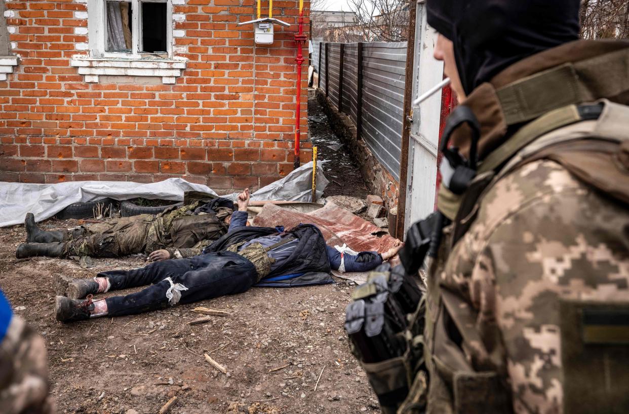 A Ukrainian soldier walks past the bodies of Russian soldiers laying on the ground after the Ukranian troops retook the village of Mala Rogan, east of Kharkiv, on March 30, 2022. 