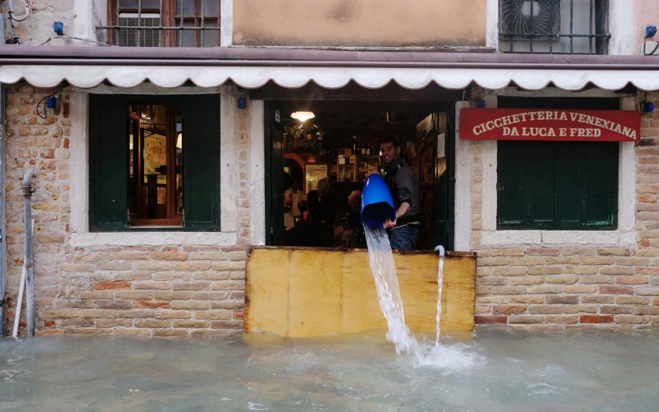 A man tips out water from a flooded restaurant in Venice - Reuters