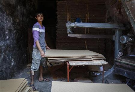 Riyazuddin, an 18-year-old worker, poses next to a cardboard box manufacturing unit at a slum in Mumbai March 23, 2014. REUTERS/Danish Siddiqui