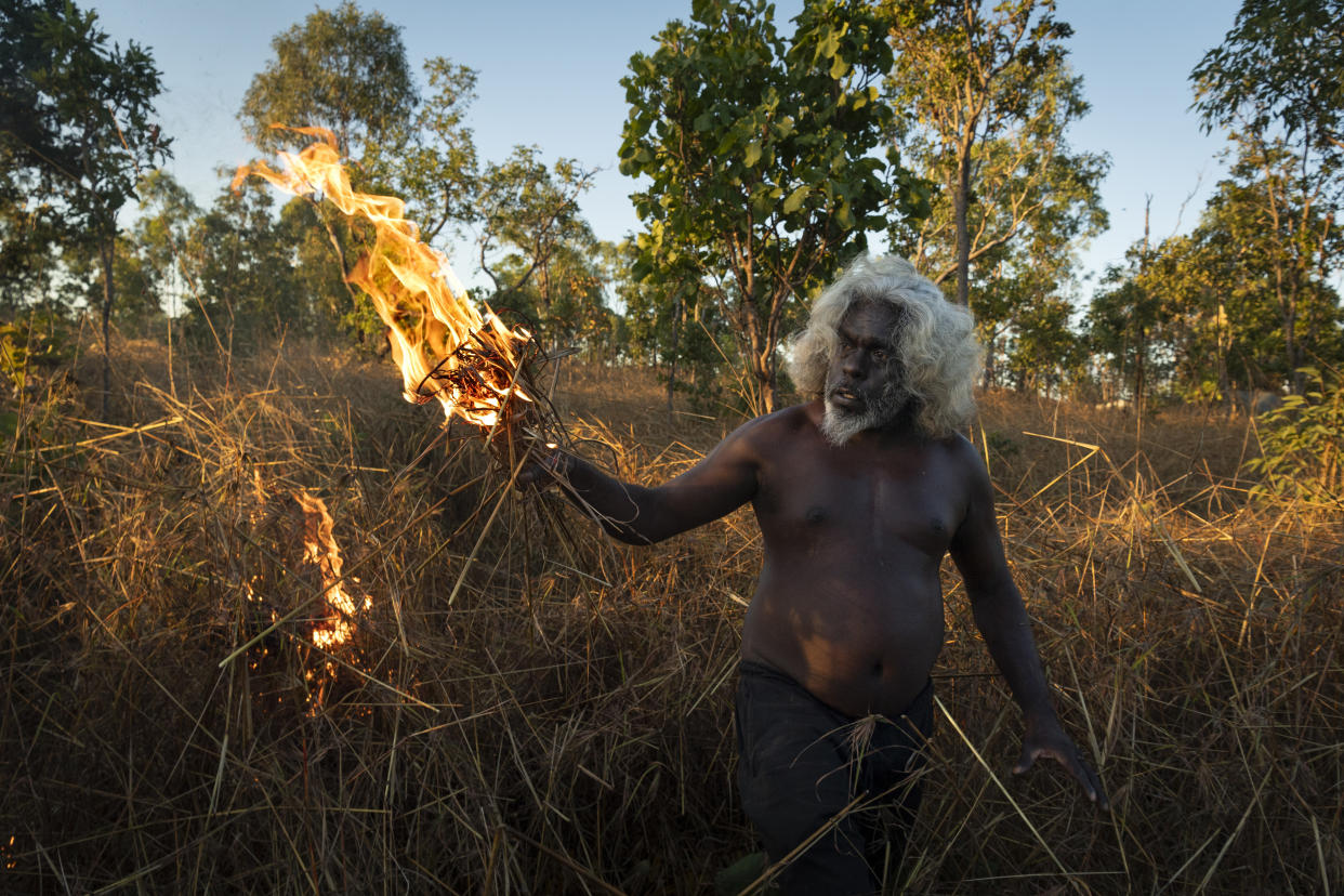 This image provided by World Press Photo which won the World Press Photo Story Of The Year award by Matthew Abbott for National Geographic Magazine/Panos Pictures, titled Saving Forests With Fire, shows Nawarddeken elder Conrad Maralngurra burns grass to protect the Mamadawerre community from late-season 'wildfires', in Mamadawerre, Arnhem Land, Australia, May 3, 2021. The late-evening fire will die out naturally once the temperature drops and moisture levels rise. (Matthew Abbott for National Geographic/Panos Pictures/World Press Photo via AP)