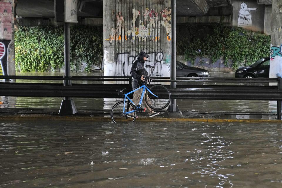 A man carries his bicycle as walks under a flooded underpass, in Athens, Thursday, Oct. 14, 2021. Storms battered the Greek capital and other parts of southern Greece, causing traffic disruption and some road closures. (AP Photo/Thanassis Stavrakis)