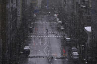 FILE - In this March 29, 2020, file, photo, a person walks in falling snow in Tokyo. Before the Olympics were postponed, Japan looked like it had coronavirus infections contained, even as they spread in neighboring countries. Now that the games have been pushed to next year, Tokyo’s cases are spiking, and the city's governor is requesting that people stay home, even hinting at a possible lockdown. (AP Photo/Eugene Hoshiko, File)