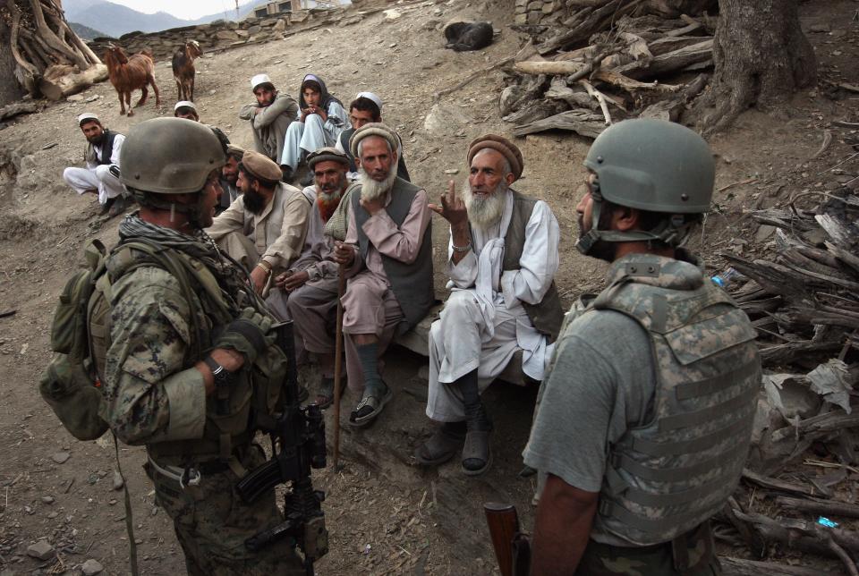 An Afghan man, wearing white, speaks to a crowd of US soldiers