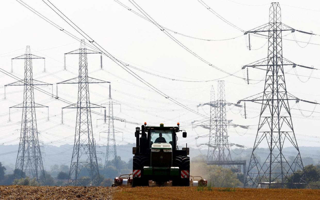 A farmer works in a field surrounded by electricity pylons - Reuters