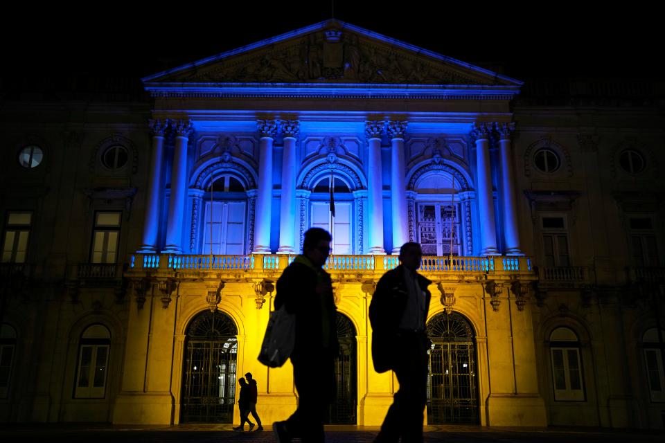 People walk in front of Lisbon's City Hall lit with the colors of the Ukrainian flag, Monday night, Feb. 28, 2022.