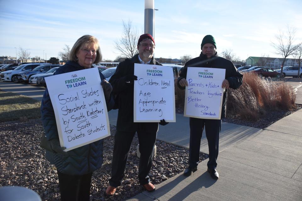 Educators stood outside the Sioux Falls Convention Center ahead of the South Dakota Board of Education Standards meeting in protest of the proposed social studies standards on Nov. 21, 2022. From left to right: Jane Leonhardt, a retired teacher, holds a sign stating "Social studies standards written by South Dakotans, for South Dakota students." Rich Mittelstedt, a former social studies teacher, holds a sign stating "Children need age appropriate learning." Loren Paul, president of the South Dakota Education Association, holds a sign stating "Parents and kids and teachers together equals better history standards."