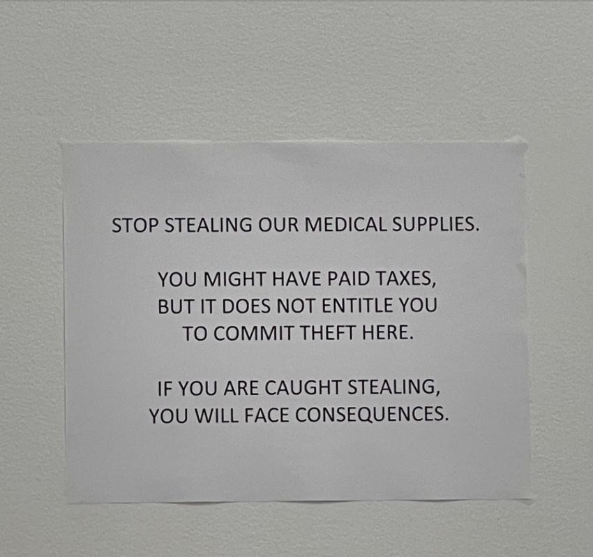 Sign on a wall reading: "STOP STEALING OUR MEDICAL SUPPLIES. YOU MIGHT HAVE PAID TAXES, BUT IT DOES NOT ENTITLE YOU TO COMMIT THEFT HERE. IF YOU ARE CAUGHT STEALING, YOU WILL FACE CONSEQUENCES."