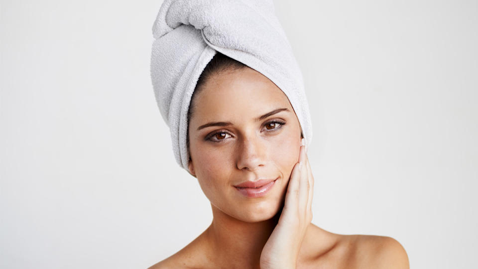 Woman with hair wrapped in a towel who is air drying her hair after learning how to air dry hair
