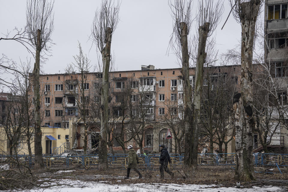 Local resident who decided to stay in the city walk on a street in front of the residential building which was heavily bombed by Russian forces in the frontline city of Vuhledar, Ukraine, Saturday, Feb. 25, 2023. (AP Photo/Evgeniy Maloletka)